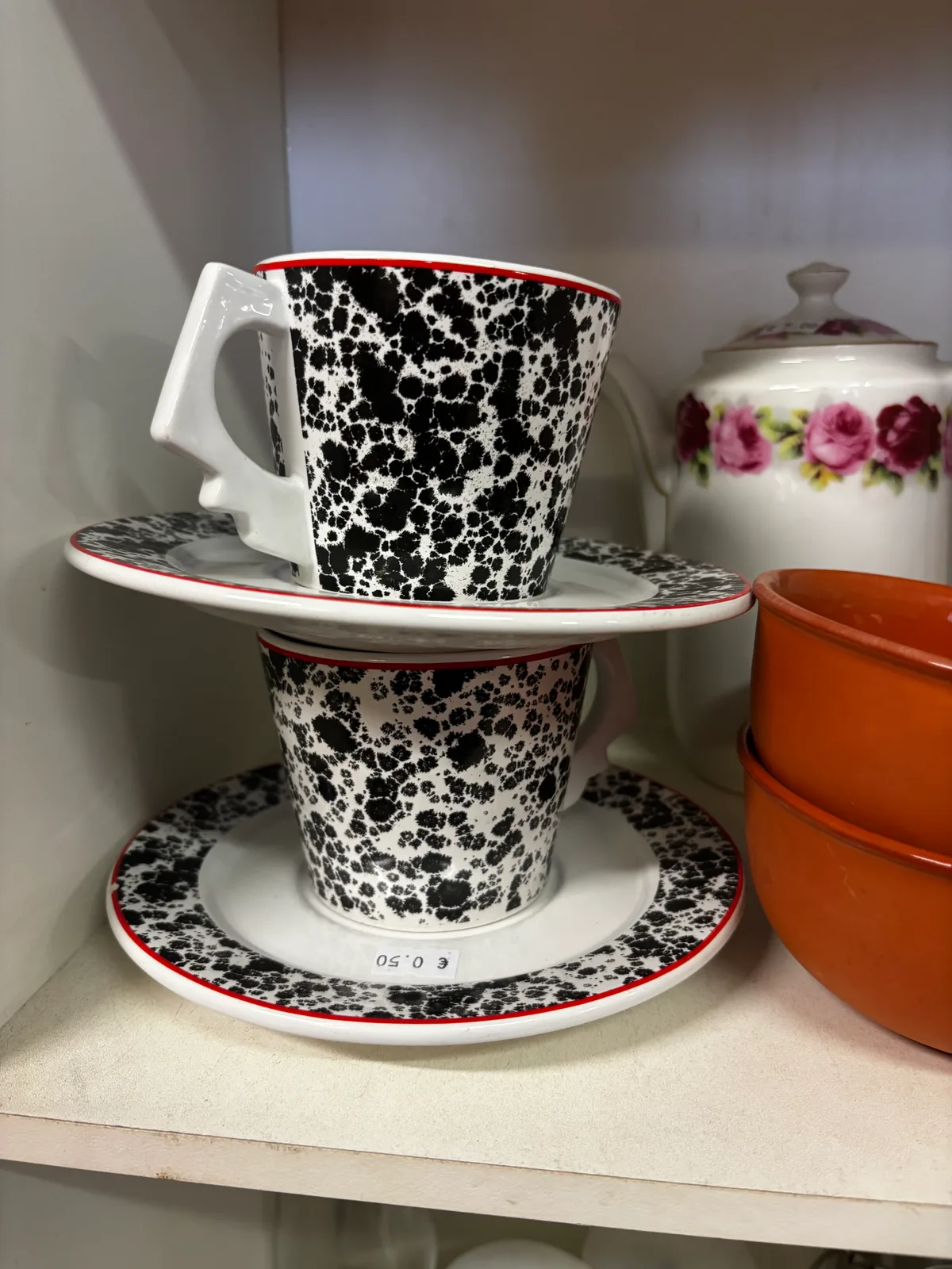 Divas keramikas krūzes ar apakštasītēm, melni baltu plankumainu rakstu un sarkanu svītriņu. 0,50 par katru priekšmetu. Nevaldāms raksts minimālos toņos un ar...